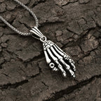 Silver skeleton hand necklace on a textured dark surface