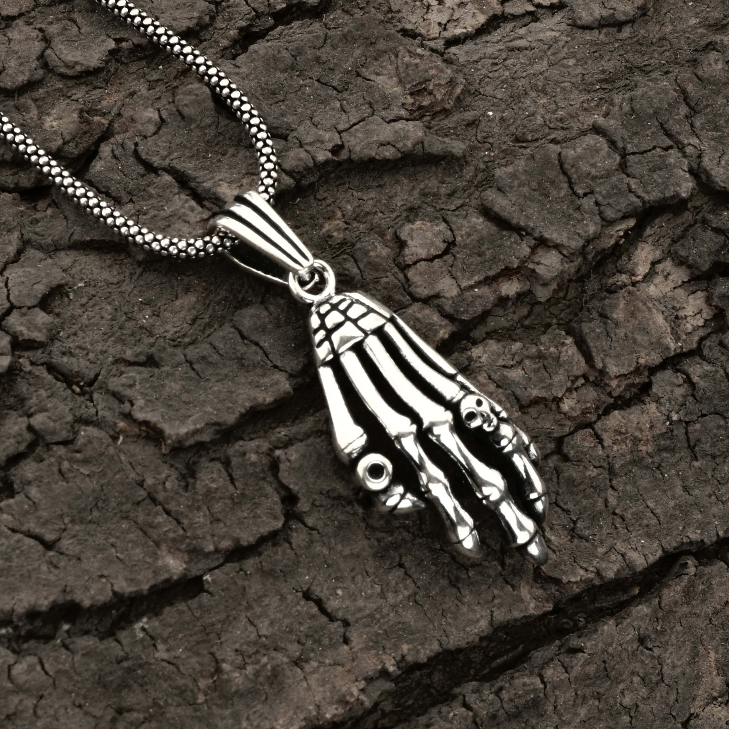 Silver skeleton hand necklace on a textured dark surface