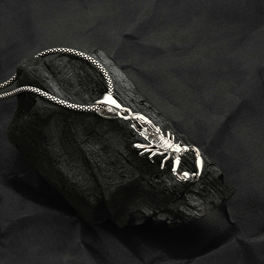 Silver scorpion pendant necklace on a dark stone surface