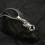 Silver scorpion pendant necklace on a dark stone surface