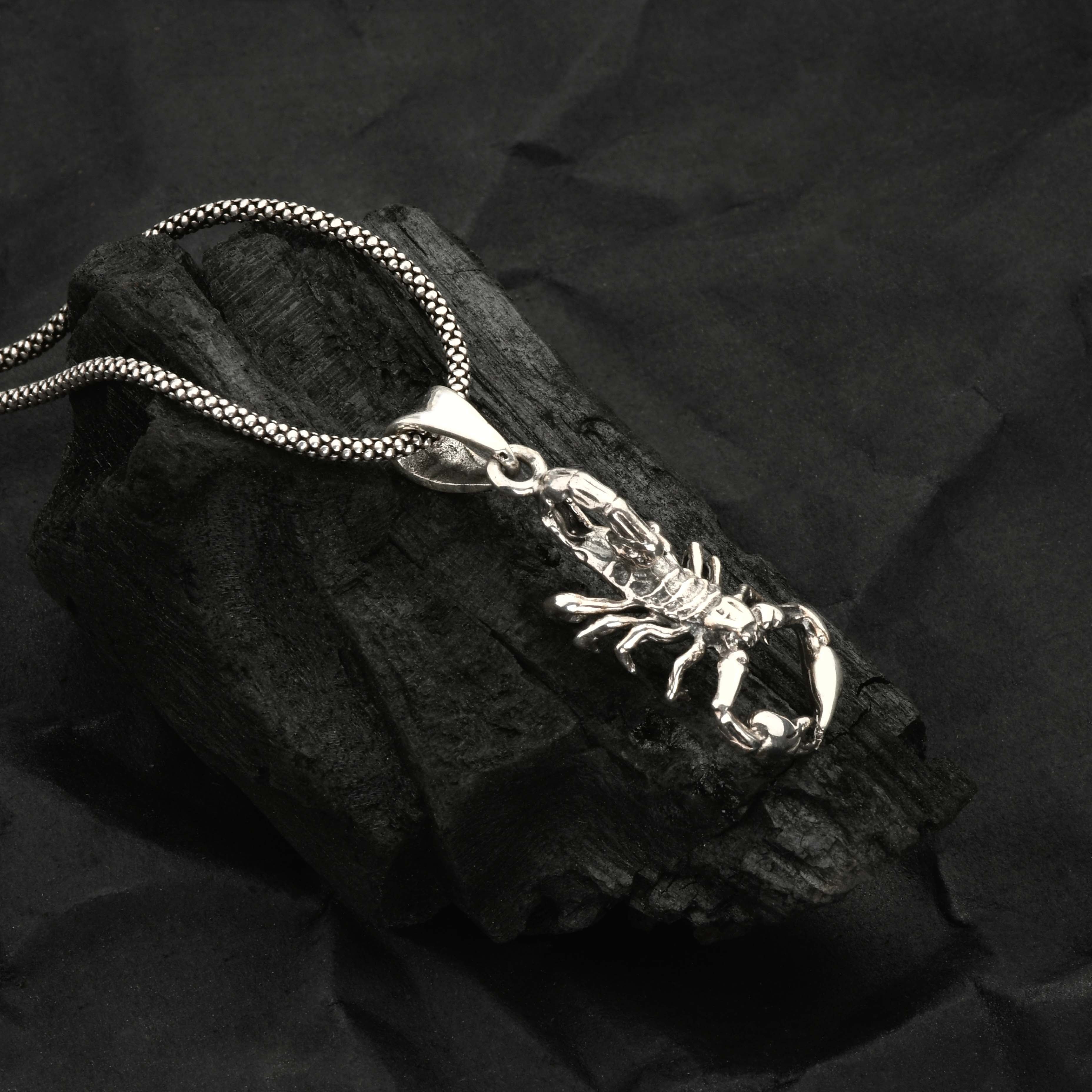 Silver scorpion pendant necklace on a dark stone surface