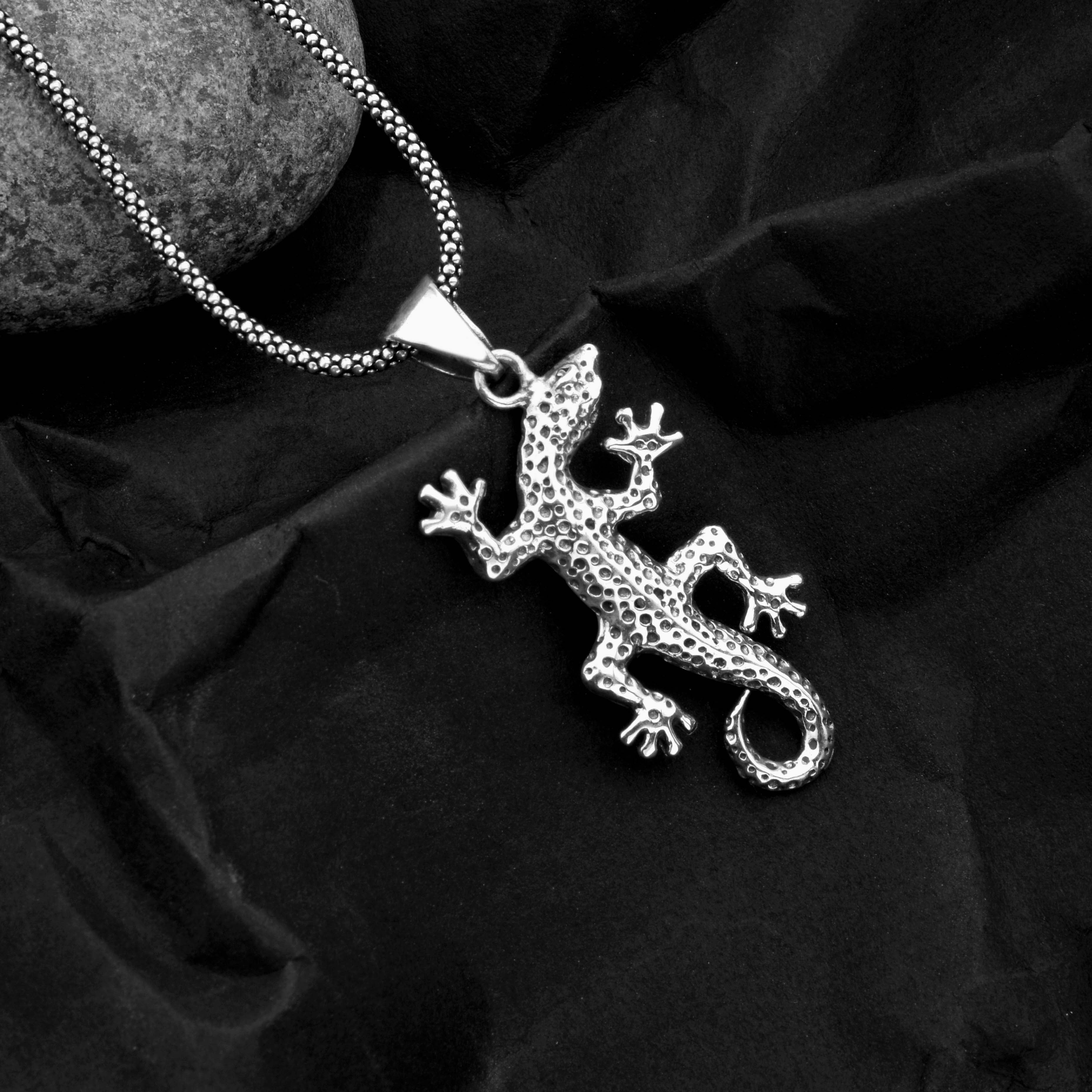 Silver lizard pendant on a chain against a black fabric background