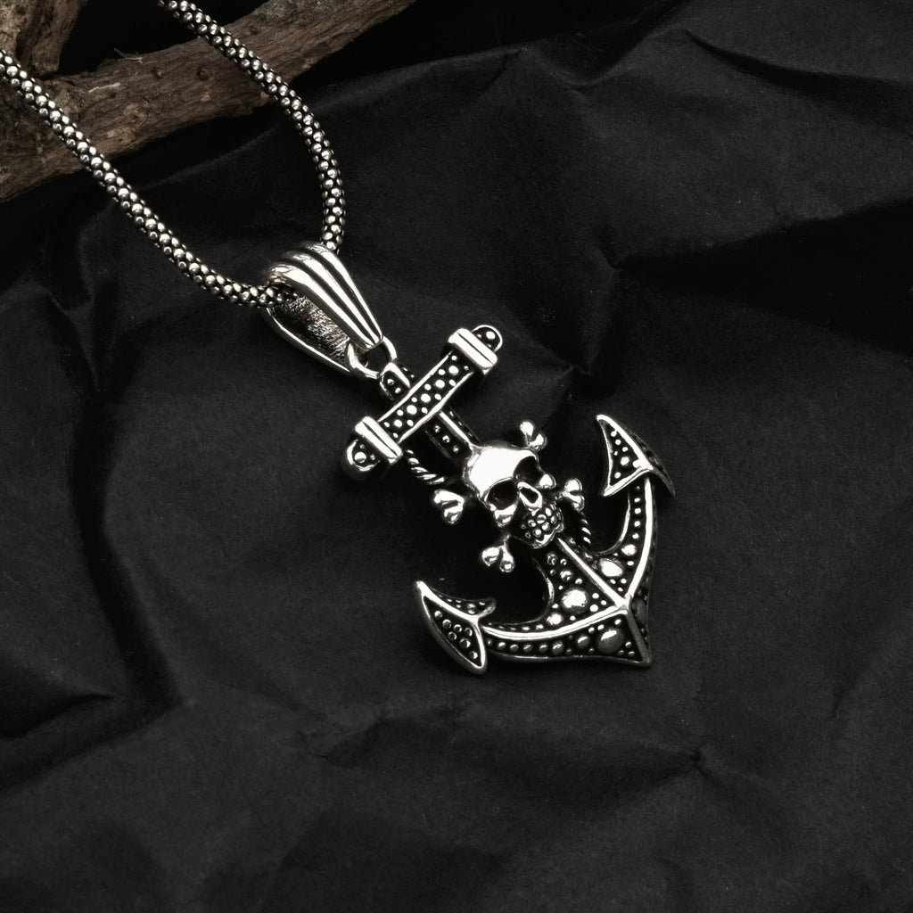 Silver pendant with anchor and skull design on a dark fabric background