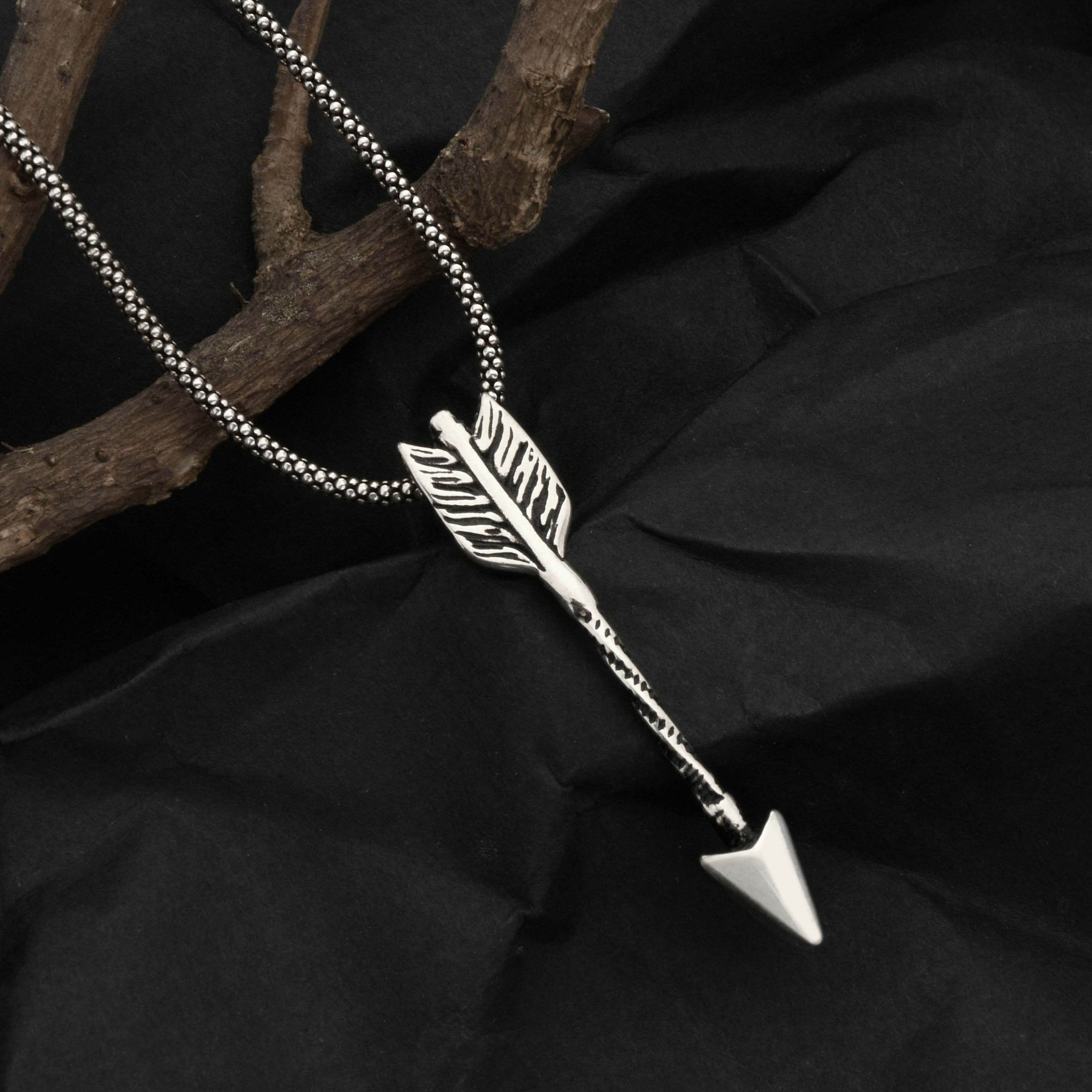 Silver arrow-shaped pendant necklace on a black fabric background