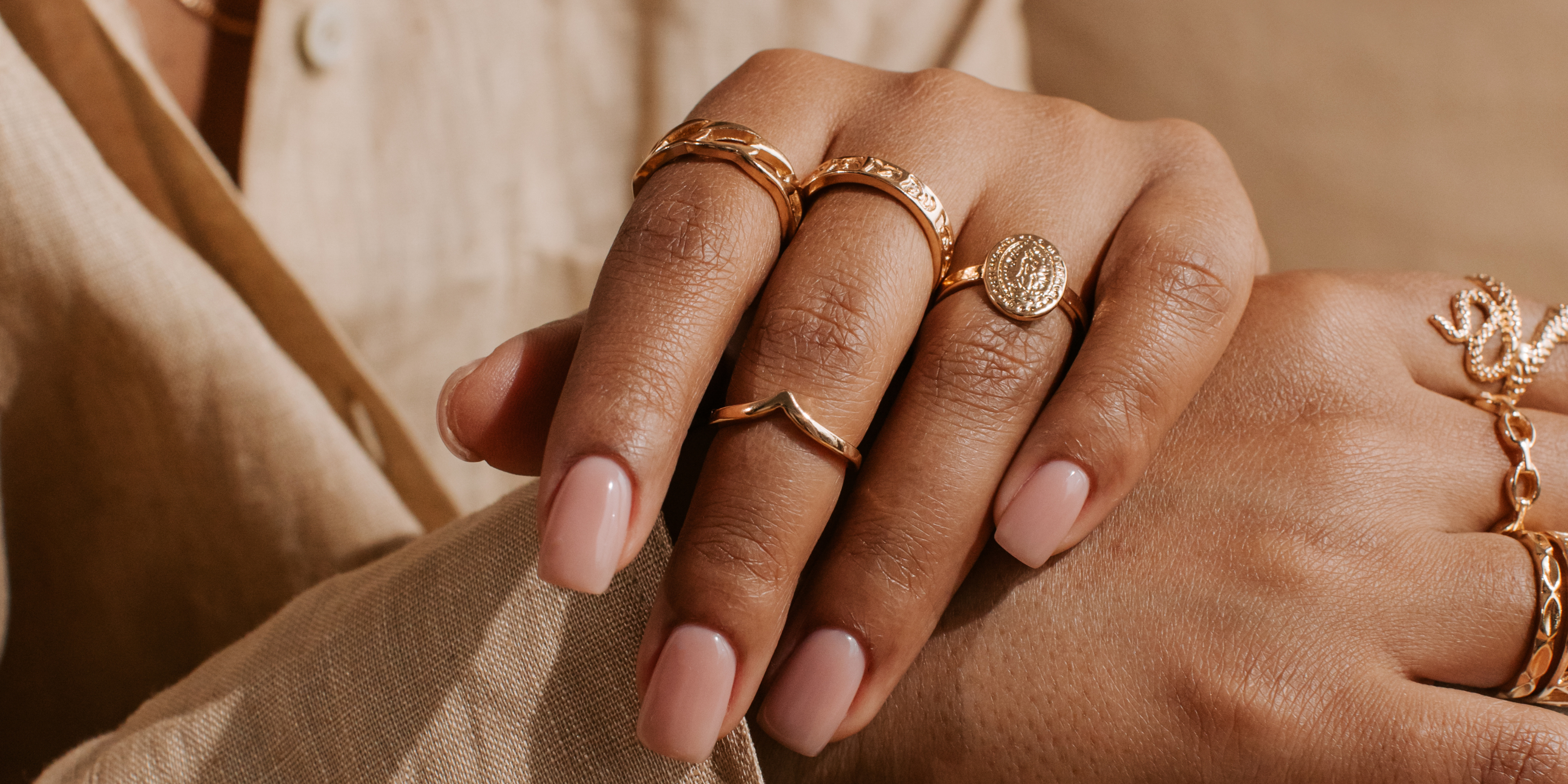 Close-up of a hand wearing multiple gold rings with a neutral background